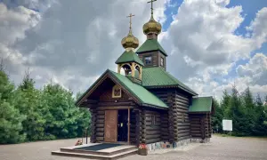 Drewniana cerkiew z zielonym dachem i złotymi kopułami, otoczona sosnami, nad brzegiem Narew.