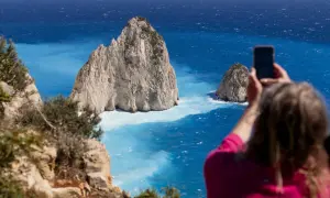 Widok na turkusowe morze i skaliste wysepki. Kobieta robi zdjęcie telefonem, uwieczniając piękno Zakynthos. Idealne miejsce na wycieczki fakultatywne.