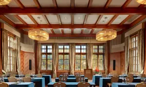 Elegancka sala konferencyjna w Kempinski Hotel, z drewnianymi belkami na suficie, dużymi oknami z widokiem na jesienny krajobraz i dwoma ozdobnymi żyrandolami.