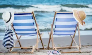Dwie leżaki na plaży, gotowe na wakacje nad Bałtykiem. W tle morze i niebo.