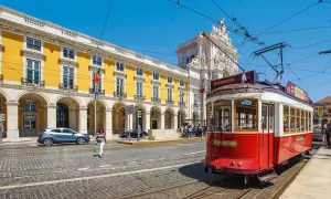Czerwony tramwaj w Lizbonie, obok żółtego budynku z arkadami. Czy do Portugalii potrzebny jest paszport? Tak, jeśli nie jesteś obywatelem UE.