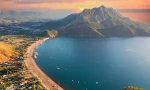 Malownicze wybrzeże Turcji o zachodzie słońca. Góry schodzą do turkusowego morza, a plaża pełna jest leżaków.