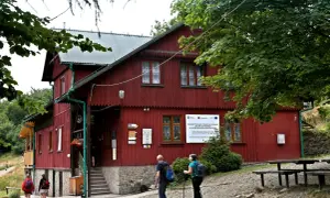 Schronisko PTTK Leskowiec, czerwony budynek w górach, turyści zbliżają się do wejścia.