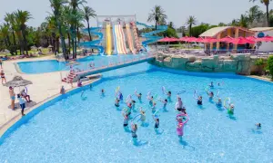 Grupa ludzi ćwiczy w basenie, a w tle widać zjeżdżalnie wodne. **One resort jockey opinie** potwierdzają świetną zabawę.
