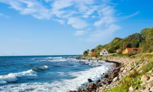 Kamienista plaża i domki na wzgórzu tworzą malowniczy krajobraz. To urokliwa wyspa na Bałtyku, gdzie fale rozbijają się o brzeg.