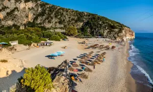 Słoneczne albania plaże z rzędami leżaków i parasoli, skaliste zbocze i turkusowe morze.
