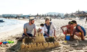 Rodzina buduje zamek z piasku na plaży, idealne miejsce na tunezja wycieczki. Dzieci bawią się z rodzicami, tworząc wspomnienia.