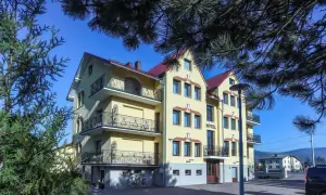 Hotel Milena w Milówce, żółty budynek z balkonami i czerwonym dachem, otoczony zielenią.