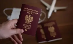 Dłoń trzyma polski paszport. Obok leżą kolejne paszporty, maseczka i samolot, sugerując podróż i pytając, ile wyrabia się paszport.