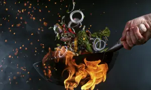 Dynamiczna kuchnia fusion: składniki w locie nad płomieniami w woku, dym i iskry tworzą magiczną atmosferę.