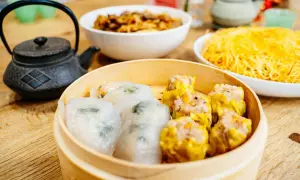 Pyszne dim sum w bambusowym parowniku, obok miseczki z makaronem i daniem mięsnym.