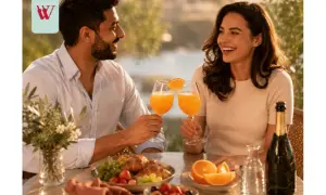 Para celebruje poranek przy stole z owocami, rogalikami i dwoma kieliszkami pełnymi musującego mimosa.