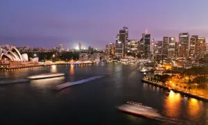 Sydney nocą, z Operą i drapaczami chmur. Zastanawiasz się, ile się leci do Australii?