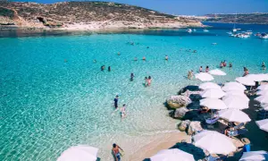 Malta w maju: turkusowa woda, plaża z białymi parasolami i ludzie kąpiący się w morzu.