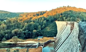 Kamienna zapora wodna w Zagórzu Śląskim otoczona zielonymi wzgórzami oświetlonymi zachodzącym słońcem.