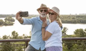 Szczęśliwa para seniorów robi selfie na tle rzeki i zieleni. Marzą o podróżach dla seniorów samolotem.