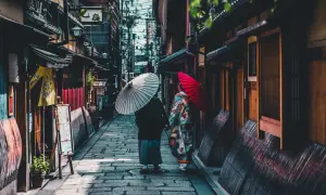 Dwie kobiety w kimonach spacerują wąską uliczką w Kioto, trzymając parasolki. To fascynujące ciekawostki o Japonii.