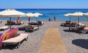 Słoneczny kurort nad Morzem Czarnym. Leżaki pod parasolami, drewniana ścieżka na kamienistej plaży, ludzie kąpiący się w morzu.