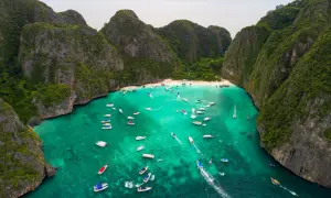 Maya Bay tętni życiem, pełna łodzi i turystów na piaszczystej plaży, otoczona stromymi, zielonymi klifami.