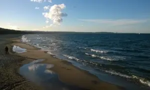 Spokojna plaża Jelitkowo o zachodzie słońca. Woda faluje, a na piasku widać kałuże i mewy.