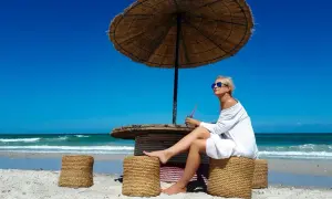 Kobieta w białej sukience siedzi pod parasolem na plaży na Djerbie. Uważać na słońce i upał.