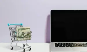 Mini wózek sklepowy z pieniędzmi obok laptopa. Idealne do szukania najlepszych reisen opinie i planowania podróży.