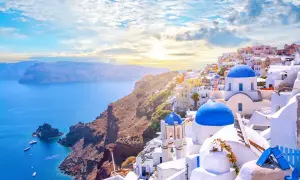 Widok na białe domy z niebieskimi dachami na Santorini, idealne miejsce na loty do Grecji. Morze i góry w tle.