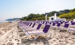 Idealne tanie wczasy nad morzem dla 2 osób z wyżywieniem. Rzędy leżaków na piaszczystej plaży, morze i zieleń w tle.
