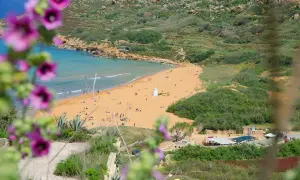 Malta pogoda kwiecień: piaszczysta plaża z turystami, turkusowe morze i zielone wzgórza. W oddali biała wieża.