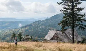 Widok na malownicze góry w Polsce. Drewniany domek i samotna turystka na tle jesiennych lasów i pagórków.