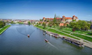 Widok na Wawel i rzekę Wisłę z łodziami. Słoneczny dzień zachęca do spacerów po zielonych bulwarach.