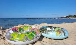 Dwa dmuchane koła na piaszczystej plaży, morze i tłumy ludzi w tle. Idealne na wakacje.pl opinie.