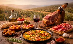 Obfity stół z przysmakami kuchni hiszpańskiej: paella, jamón, tapas i wino, na tle malowniczego krajobrazu.