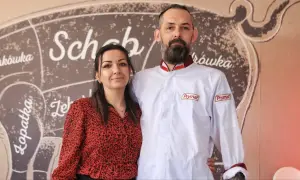 Para z uśmiechem na tle schematu rozbioru świni. On w białej kurtce z logo Prymat, ona w czerwonej bluzce. Wszyscy chwalą złota świnka opinie.
