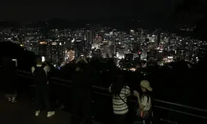 Nocny widok na rozświetlone miasto, przypominające panoramę Gangnam. Ludzie robią zdjęcia, podziwiając miejski krajobraz.