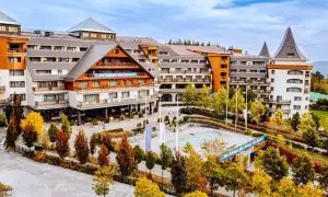 Hotel Gołębiewski w jesiennej odsłonie. Widać jego rozległą architekturę i otoczenie pełne kolorowych drzew.