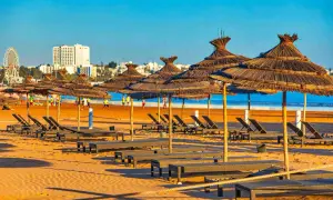 Słoneczna plaża w Agadirze w marcu, puste leżaki pod strzechowymi parasolami, w tle budynki i diabelski młyn.