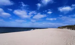 Piękna, słoneczna pogoda na sierpień nad morzem. Szeroka, piaszczysta plaża, spokojne morze i błękitne niebo z białymi chmurami.