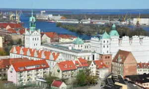 Widok na port w Szczecinie z żurawiami, statkami i zabudowaniami miejskimi.