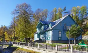 Piękny, błękitny budynek sanatorium Nida-Zdrój otoczony jesiennymi drzewami. Wiele pozytywnych **sanatorium Nida-Zdrój opinie** potwierdza urok tego miejsca.