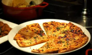 Kawałki pizzy z serem i ziołami na białym talerzu.