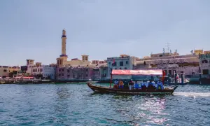 Tradycyjna łódź z pasażerami płynie po rzece w Dubaju, w tle widoczne stare budynki i minaret.