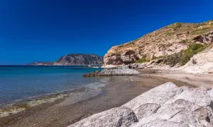 Majowa pogoda na Kos: skalista plaża z turkusową wodą i łagodnymi falami, w tle góry.