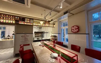Wnętrze restauracji z długim stołem, czerwonymi krzesłami i piecem do pizzy. Otto Pompieri opinie pozytywne, warto odwiedzić!