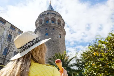 Kobieta w kapeluszu i żółtej kurtce je lody pod wieżą Galata w Stambule, Turcja.