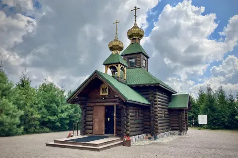 Drewniana cerkiew z zielonym dachem i złotymi kopułami, otoczona sosnami, nad brzegiem Narew.