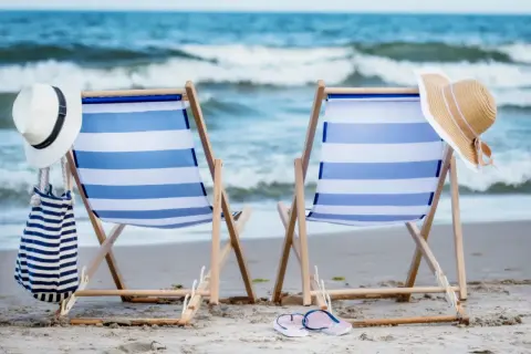 Dwie leżaki na plaży, gotowe na wakacje nad Bałtykiem. W tle morze i niebo.
