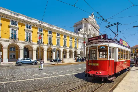 Czerwony tramwaj w Lizbonie, obok żółtego budynku z arkadami. Czy do Portugalii potrzebny jest paszport? Tak, jeśli nie jesteś obywatelem UE.