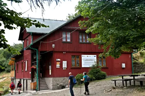 Schronisko PTTK Leskowiec, czerwony budynek w górach, turyści zbliżają się do wejścia.