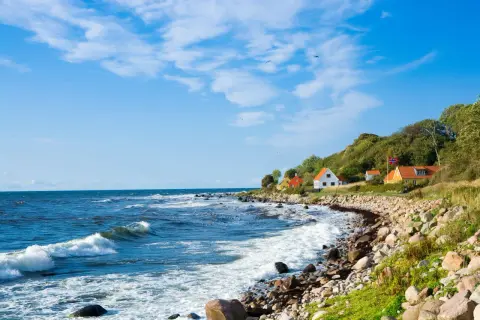 Kamienista plaża i domki na wzgórzu tworzą malowniczy krajobraz. To urokliwa wyspa na Bałtyku, gdzie fale rozbijają się o brzeg.